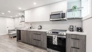 A modern kitchen with white cabinets, a built-in microwave, a stove, and a coffee maker. - Luxury Suite by Kensington Market Downtown Toronto (Toronto)