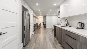 A modern kitchen with white cabinets, a stainless steel refrigerator, a dining area with a table and chairs, and a coffee maker on the counter. - Luxury Suite by Kensington Market Downtown Toronto (Toronto)
