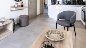 A modern kitchen with white cabinets and a marble backsplash, a dining area with a wooden table and a woven basket, and a grey chair. - Bianco Mare Studios-Apartments (Kalyves Polygyrou)