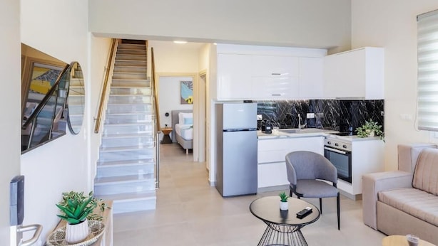 A modern kitchen with white cabinets, a black marble backsplash, and a dining area with a round table and two chairs. - Bianco Mare Studios-Apartments (Kalyves Polygyrou)