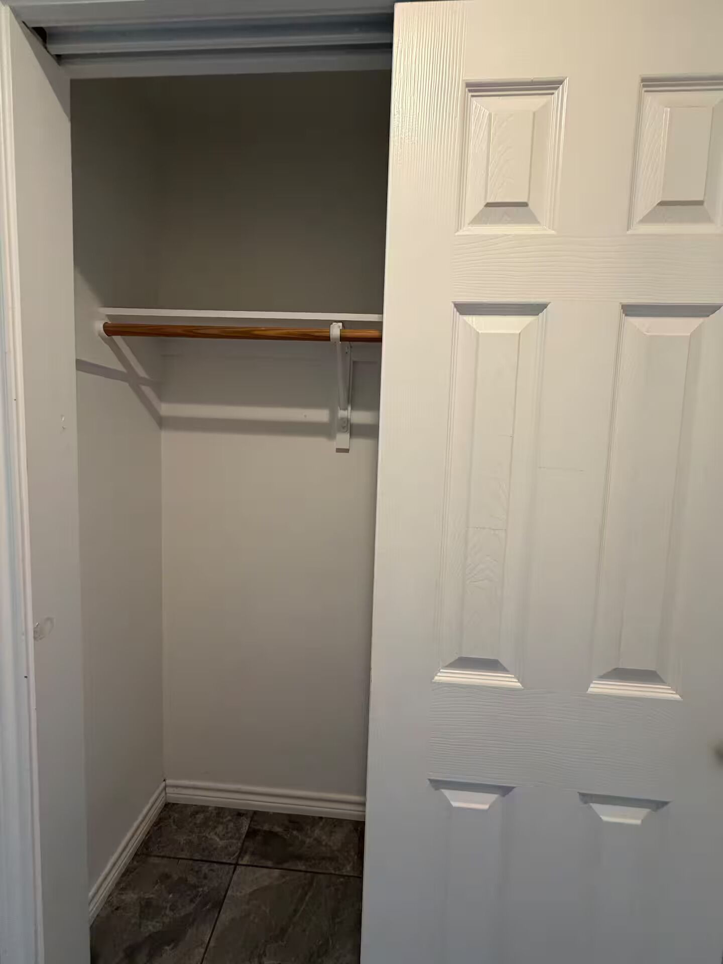 Un armario con barra de madera, una puerta blanca con paneles y suelo de baldosas.
