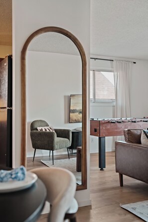 Ein modernes Wohnzimmer mit einem Kicker, einer Couch, einem Sessel und einem Esstisch.