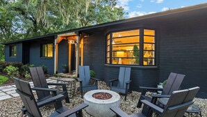 Een modern huis met een vuurkorf, buiten zitplaatsen en een groot raam.