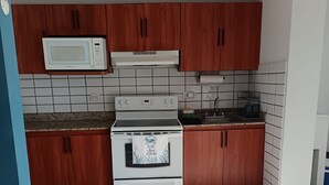 Een keuken met houten kastjes, een witte oven, een magnetron en een betegelde spatwand.