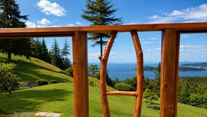 A wooden deck with a view of a grassy landscape and a body of water. - Sweeping Pacific Views & Unforgettable Sunsets · Your Island Escape, 20 Min Away (Bowen Island)