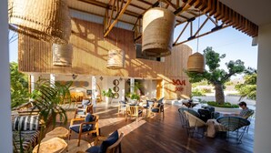 A spacious indoor area with wooden flooring, wicker furniture, and hanging light fixtures. - Tropical Ocean Breeze Retreat Steps from Beach & Lagoon (Paje)