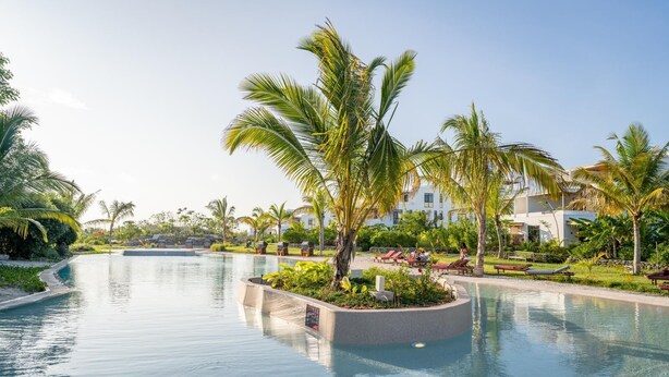 A resort pool area with palm trees, lounge chairs, and a clear sky. - Tropical Ocean Breeze Retreat Steps from Beach & Lagoon (Paje)