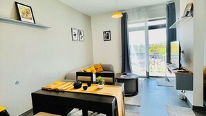 A modern living room with a dining area, a sofa, a coffee table, and a TV. - Tropical Ocean Breeze Retreat Steps from Beach & Lagoon (Paje)