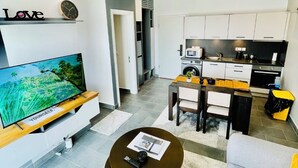 A modern apartment with a TV, sofa, dining area, kitchen, and a small balcony. - Tropical Ocean Breeze Retreat Steps from Beach & Lagoon (Paje)