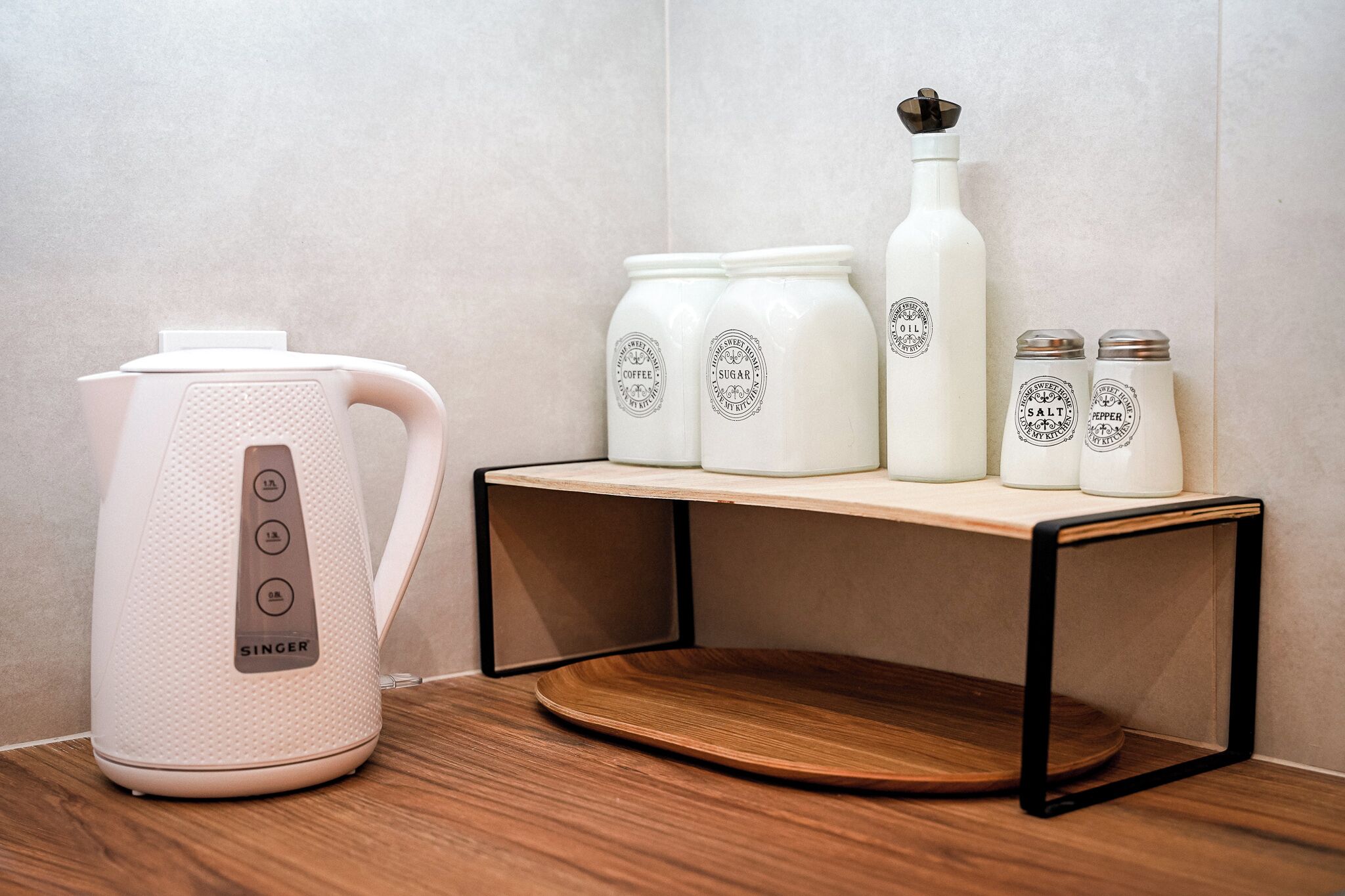 A kitchen area with a white electric kettle, sugar and coffee containers, a salt and pepper shaker, and a wooden shelf.