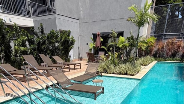 A swimming pool with a tiled deck, lounge chairs, and a building in the background.
