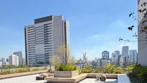 A rooftop terrace with a cityscape view, seating areas, and a large building in the background.