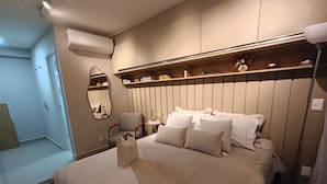 A bedroom with a large bed, a chair, a bedside table, a mirror, and a shelf with decorative items.