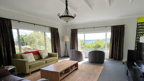 A living room with a sofa, a coffee table, a lamp, and a television. - Spacious 4 BRM home with spa and large garden (Taupō)