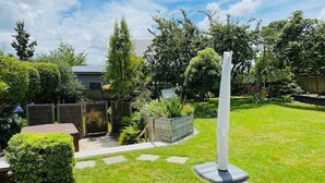 A well-maintained garden with a central white sculpture, a wooden bench, and a variety of plants. - Spacious 4 BRM home with spa and large garden (Taupō)