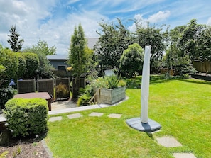 Um jardim bem cuidado com uma escultura branca central, um banco de madeira e diversas plantas.