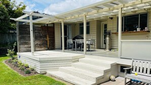 A covered patio with steps leading to a seating area, a grill, and a window overlooking the yard. - Spacious 4 BRM home with spa and large garden (Taupō)