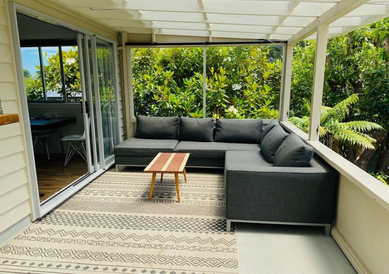 A covered outdoor seating area with a sofa and a small table, surrounded by greenery.