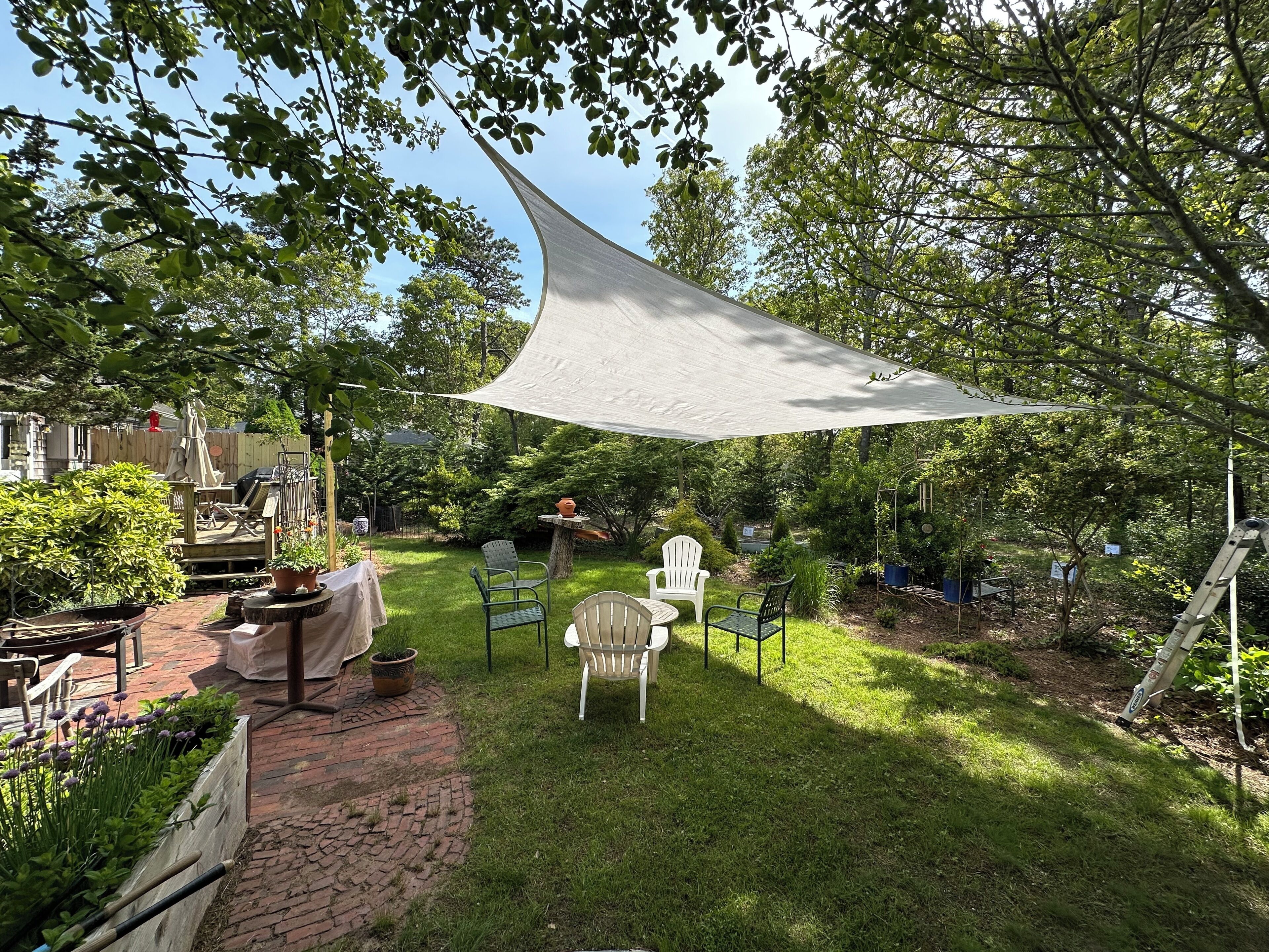 A backyard with a white shade sail, a brick pathway, and outdoor furniture.