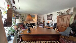 Una sala de estar con un piano de cola, chimenea, estantería y una guitarra.