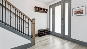 A hallway with a wooden staircase, a shoe shelf, a door with a peephole, and a framed picture on the wall. - Luxurious Newer Home - Prime Location in Downtown Pensacola - Outdoor Kitchen - Private Weight Room (Pensacola)