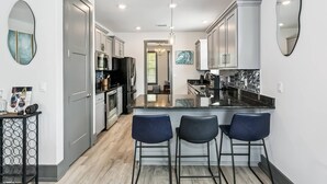 A modern kitchen with a central island, bar stools, and a view into the dining area. - Luxurious Newer Home - Prime Location in Downtown Pensacola - Outdoor Kitchen - Private Weight Room (Pensacola)