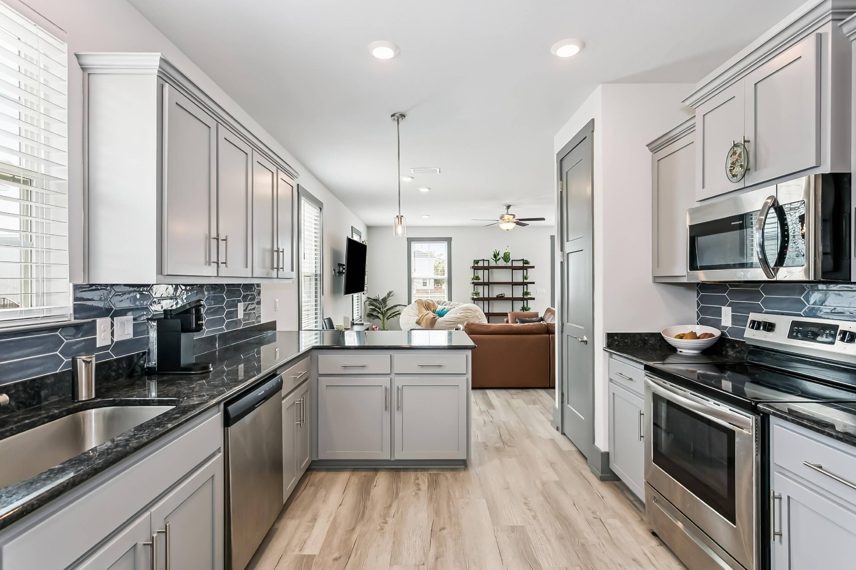 A modern kitchen with grey cabinets, a black countertop, stainless steel appliances, and a wooden floor.