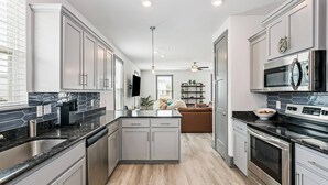 A modern kitchen with grey cabinets, a black countertop, stainless steel appliances, and a wooden floor. - Luxurious Newer Home - Prime Location in Downtown Pensacola - Outdoor Kitchen - Private Weight Room (Pensacola)