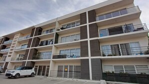 A multi-story residential building with balconies, a gated entrance, and parked cars. - Cozy 2-bedroom apartment in Cabo San Lucas. (Cabo San Lucas)