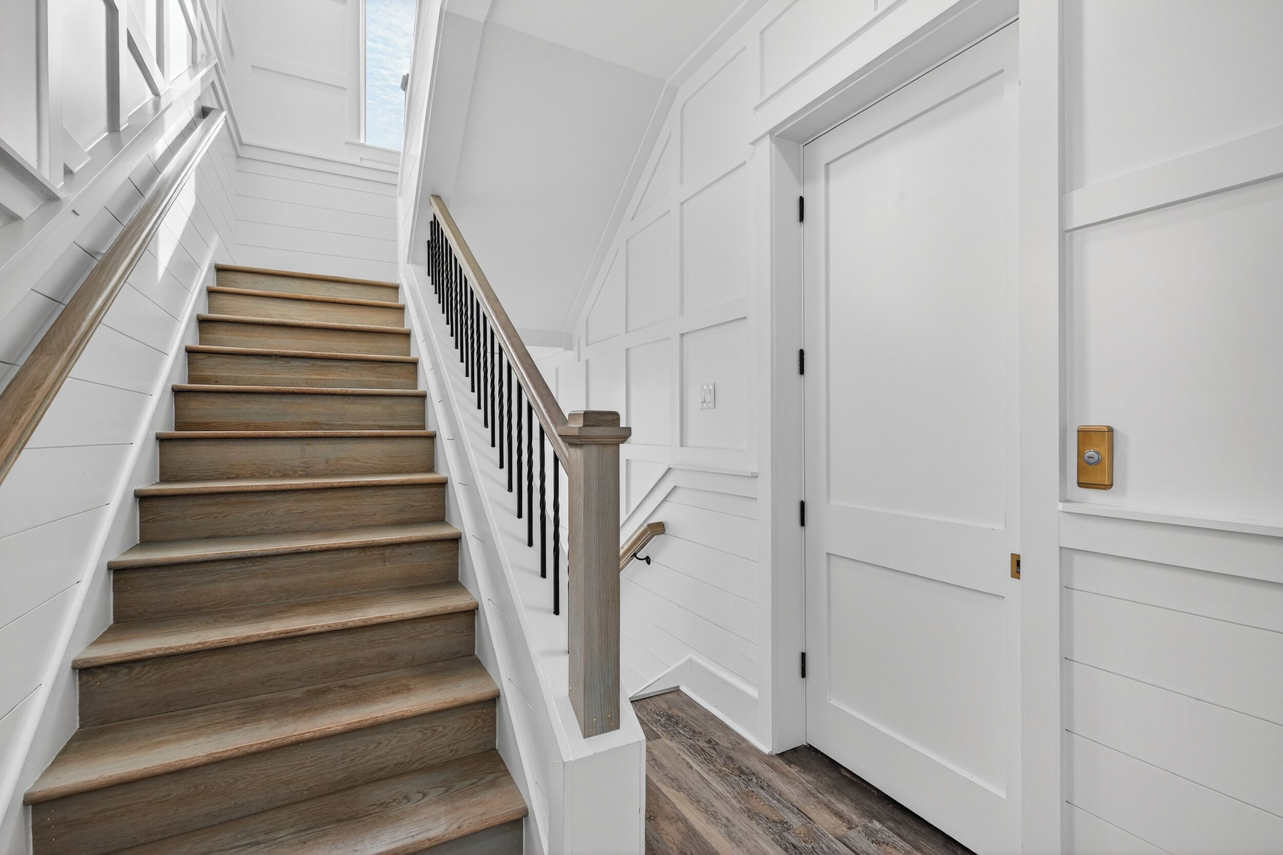 A staircase with wooden steps and a white wall with paneling.