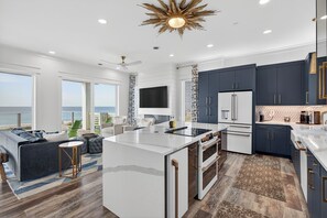 A modern kitchen with a large island, dark cabinets, and a view of the ocean. - 6BR Gulf-front Home, Sleeps 19, Heated Pool & Mini Golf (Panama City Beach)