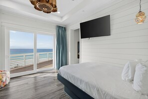 A bedroom with a large bed, a TV mounted on the wall, and a sliding glass door leading to a balcony with a view of the ocean. - 6BR Gulf-front Home, Sleeps 19, Heated Pool & Mini Golf (Panama City Beach)