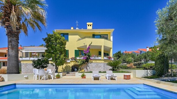 A poolside view of a yellow building with a balcony, surrounded by greenery and a clear blue sky. - Dionis apartment - 3 bedroom apartment with shared pool in a quiet neighborhood (Zadar)