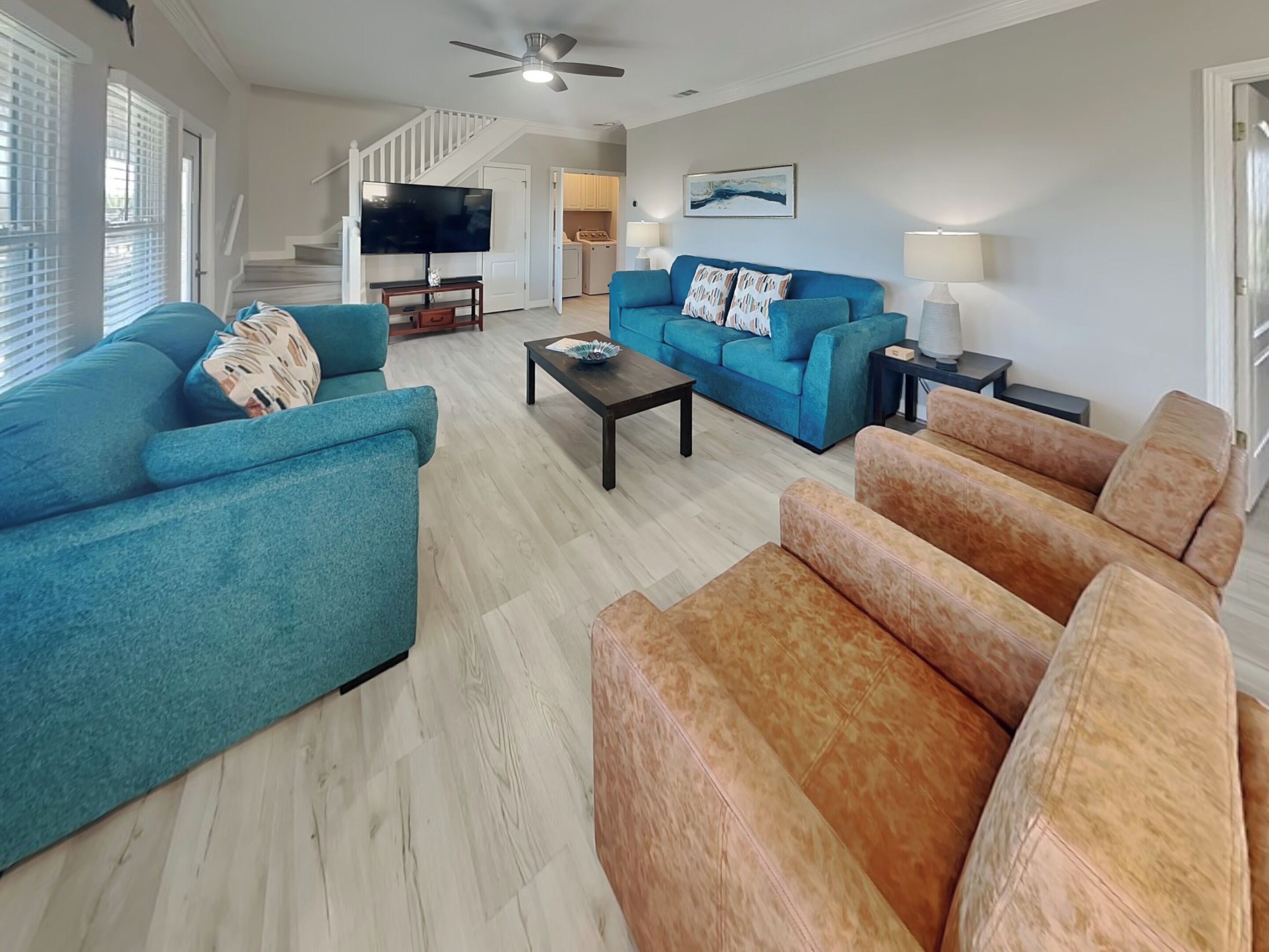 A living room with a sofa, armchairs, a coffee table, a TV, and a staircase leading to a kitchen.