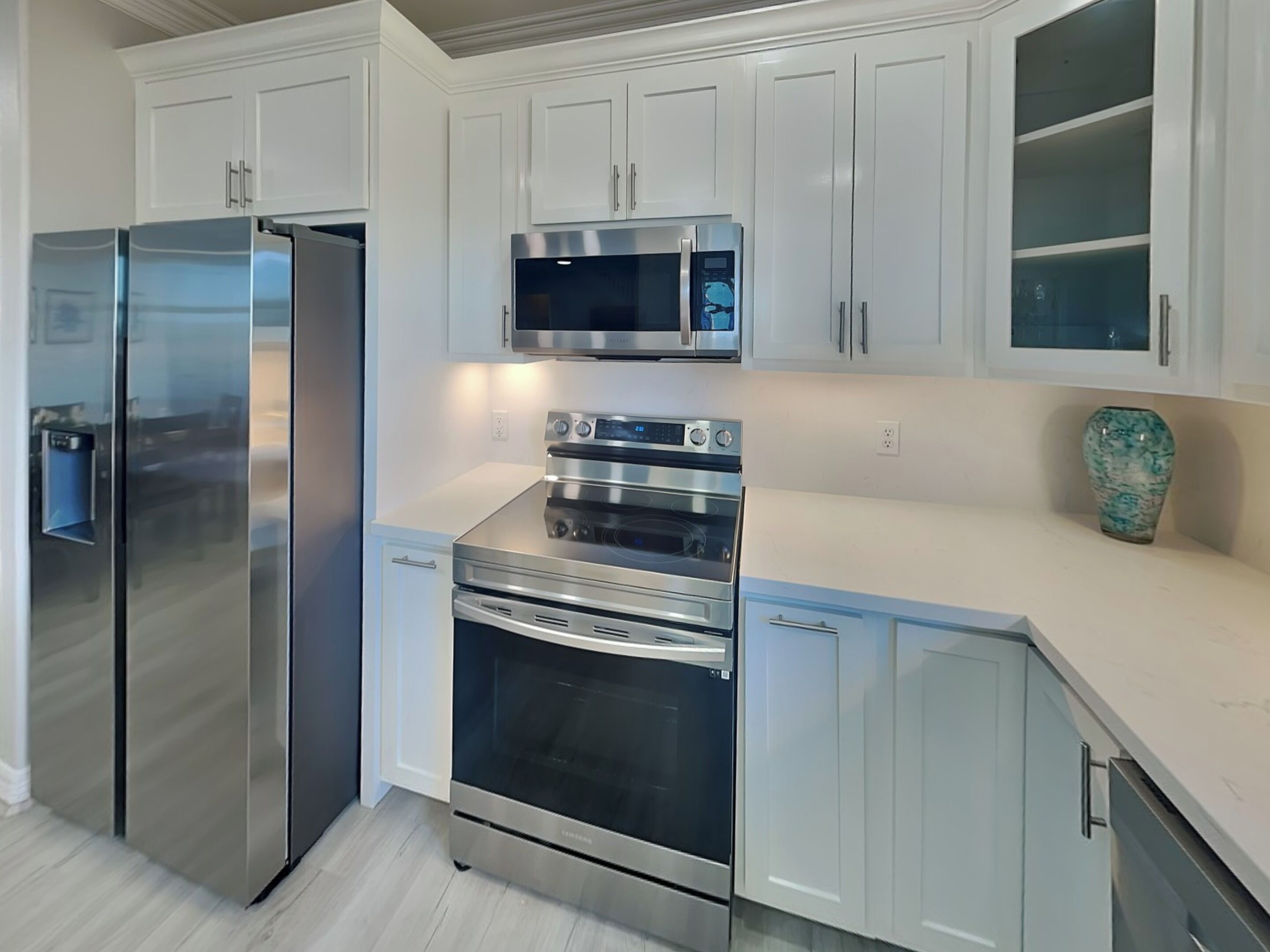 A modern kitchen with stainless steel appliances, white cabinetry, and a marble countertop.