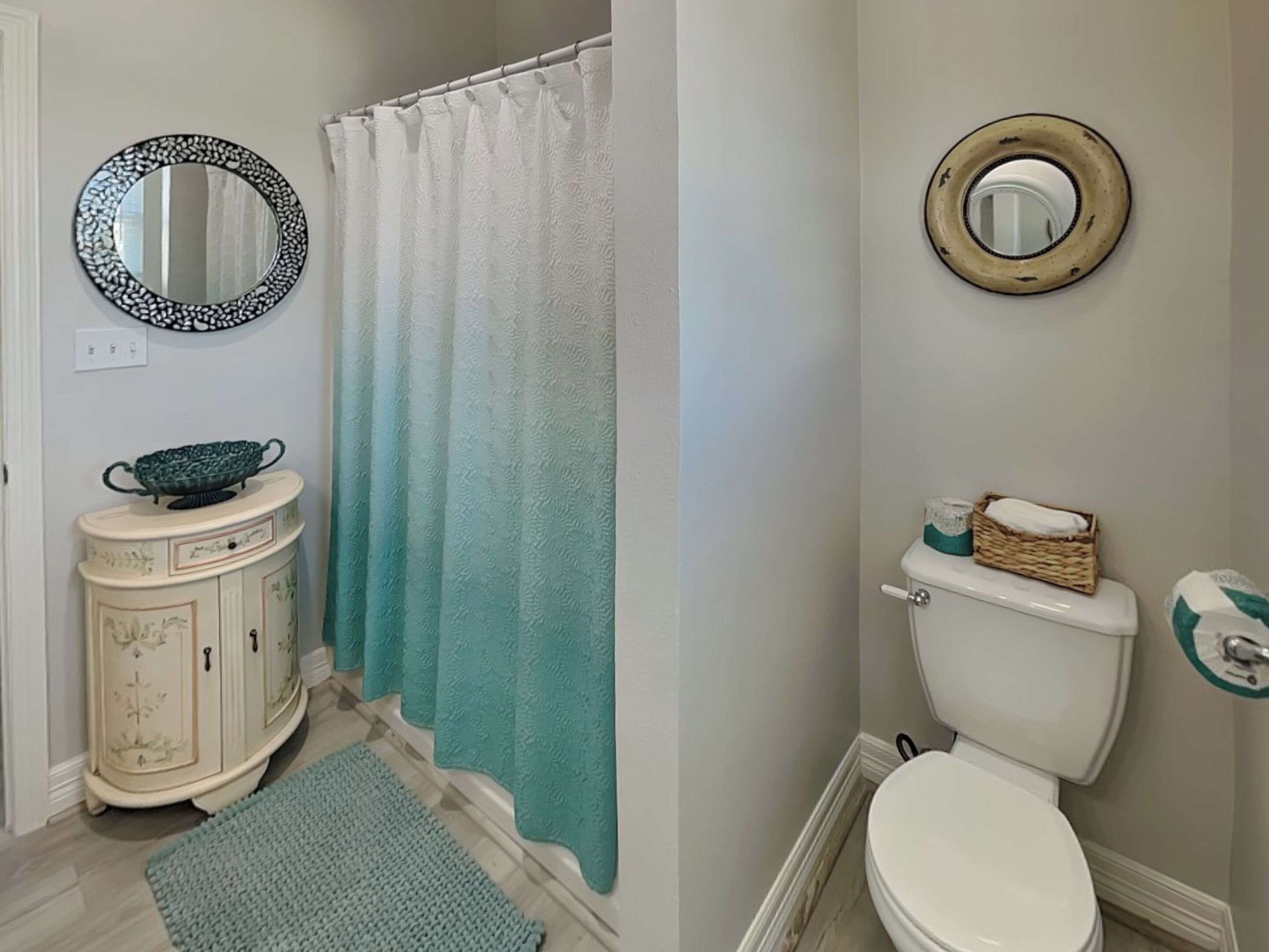 A bathroom with a white toilet, a white shower curtain, a white vanity with a green bowl, and a mirror with a black frame.