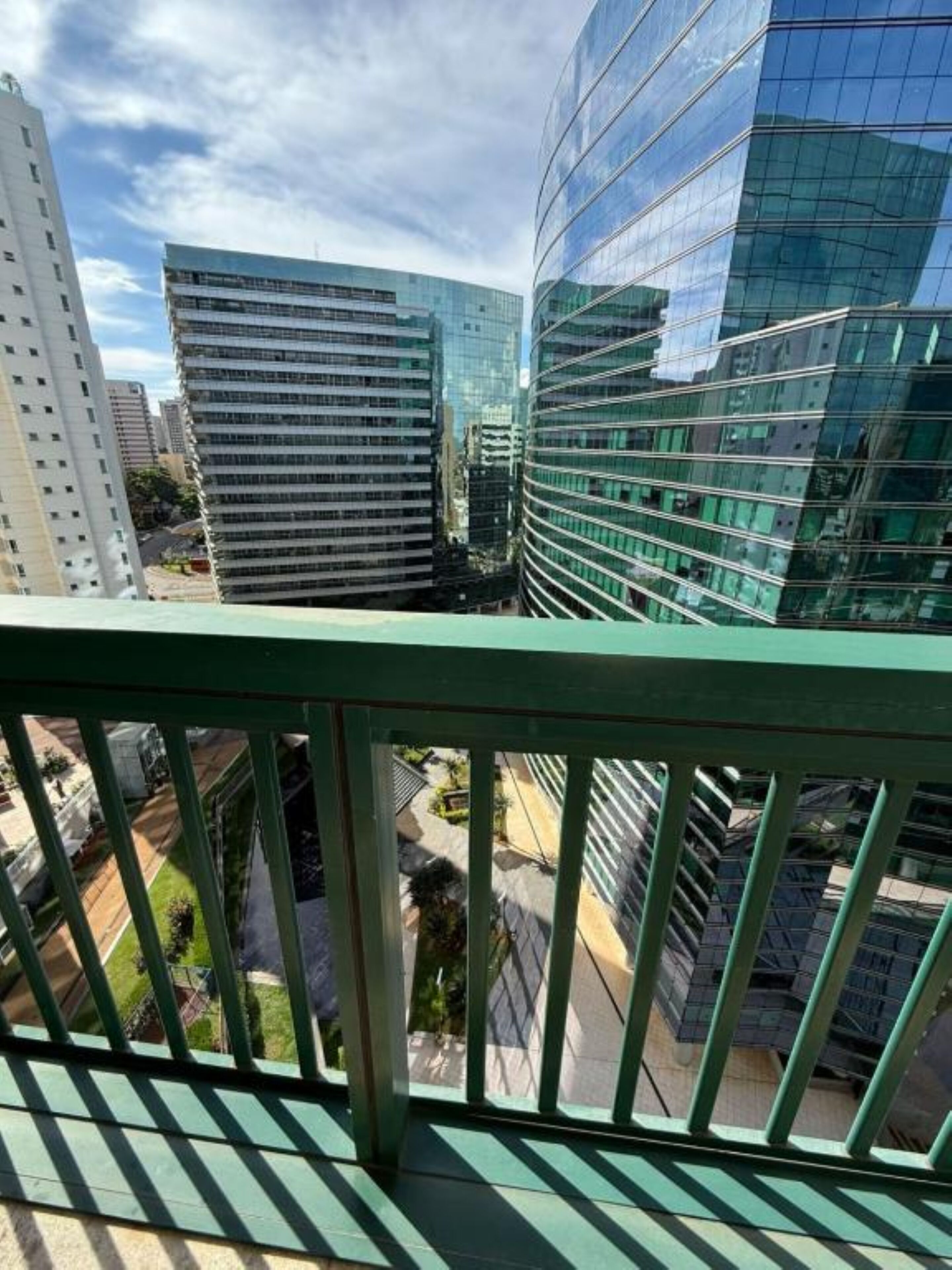 Un edificio moderno con ventanales de vidrio reflectante y barandilla de balcón verde.