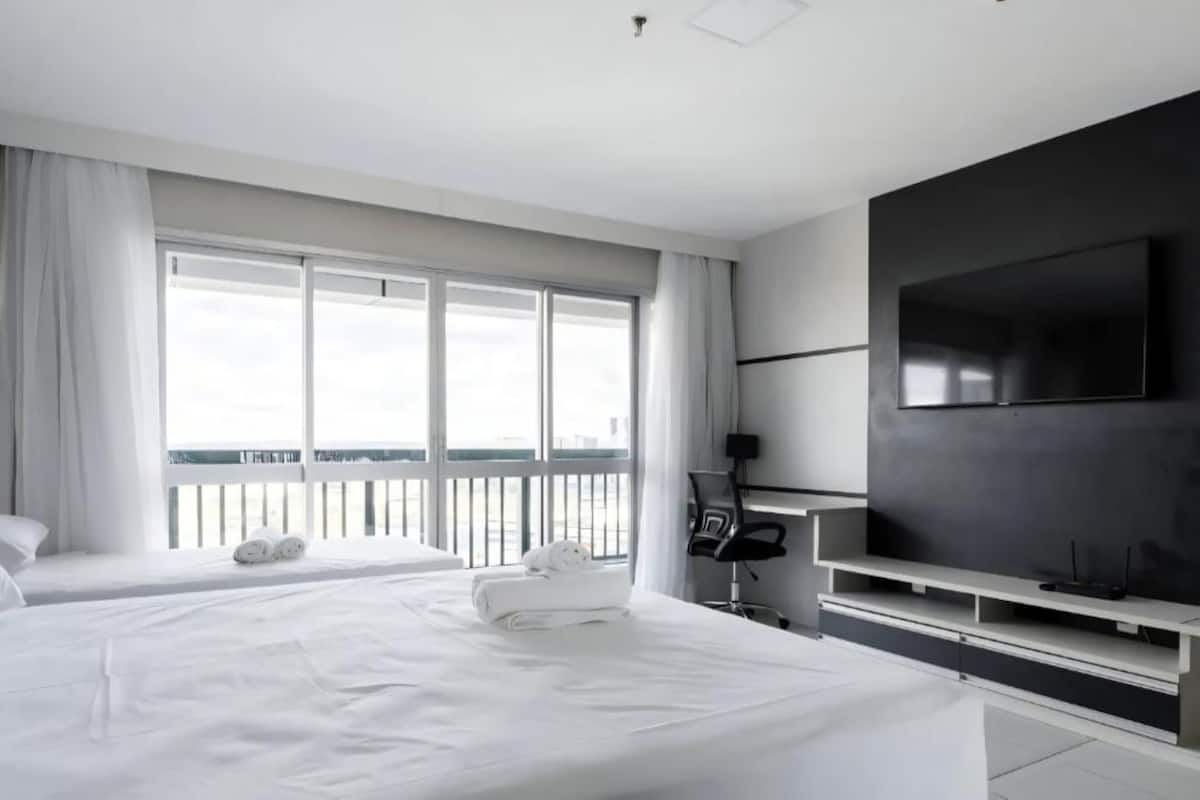 A modern hotel room with two beds, a large window, a flat-screen TV, and a balcony.