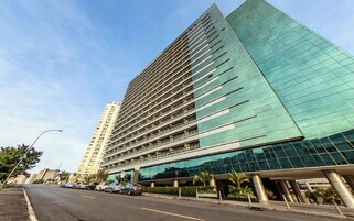 Un moderno edificio de gran altura con fachada de vidrio, varios pisos y un estacionamiento al frente.