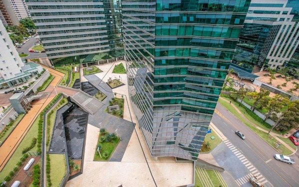 A modern high-rise building with a glass facade, surrounded by greenery and a pedestrian area.