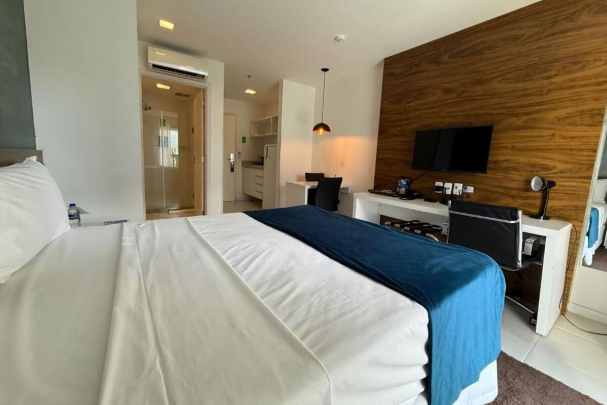 A hotel room with a bed, a desk, a television, and a wooden accent wall.