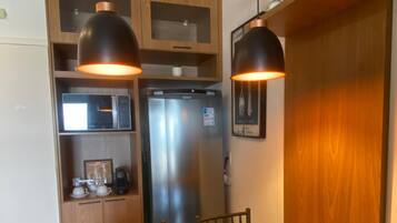 A compact kitchen with a wooden table, two chairs, a refrigerator, and pendant lights.