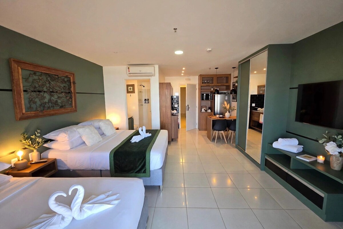 Habitación de hotel con dos camas, televisión, escritorio con silla y kitchenette.
