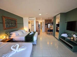 Quarto de hotel com duas camas, televisão, secretária com cadeira e cozinha compacta.