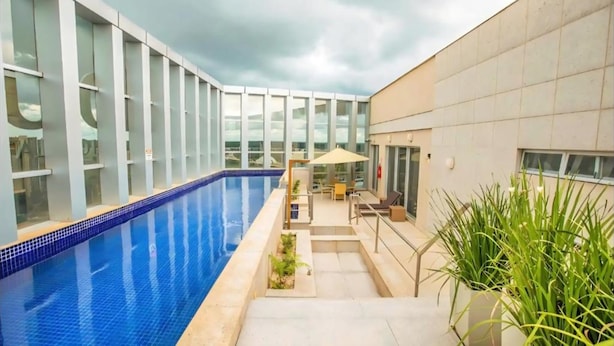 A swimming pool with a glass enclosure, a patio area with outdoor seating, and a building with large windows. - Flats Premium com vista Incrível no hotel Vision (Brasília)