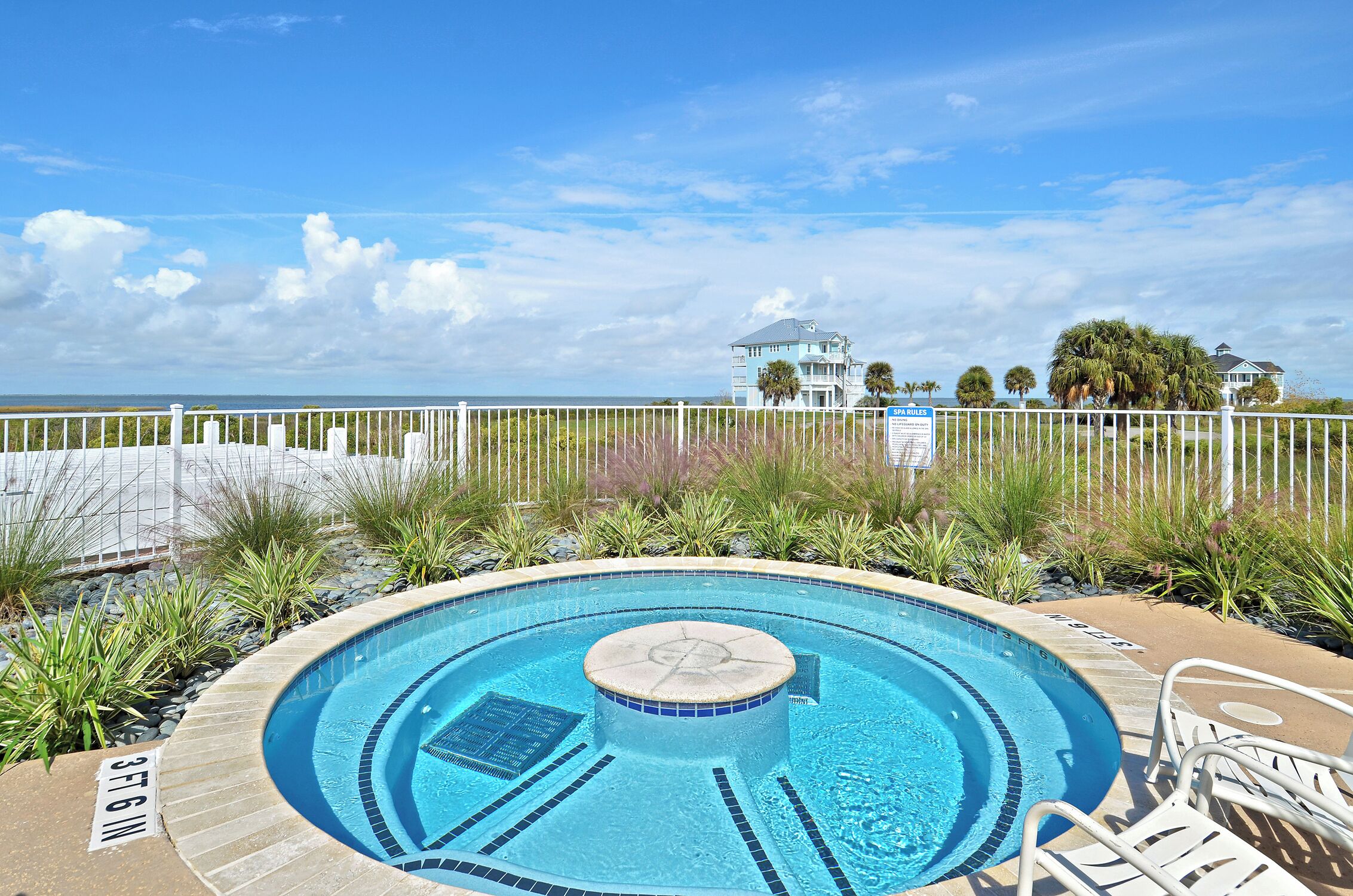 A swimming pool with a circular design, surrounded by a white fence and tropical plants.