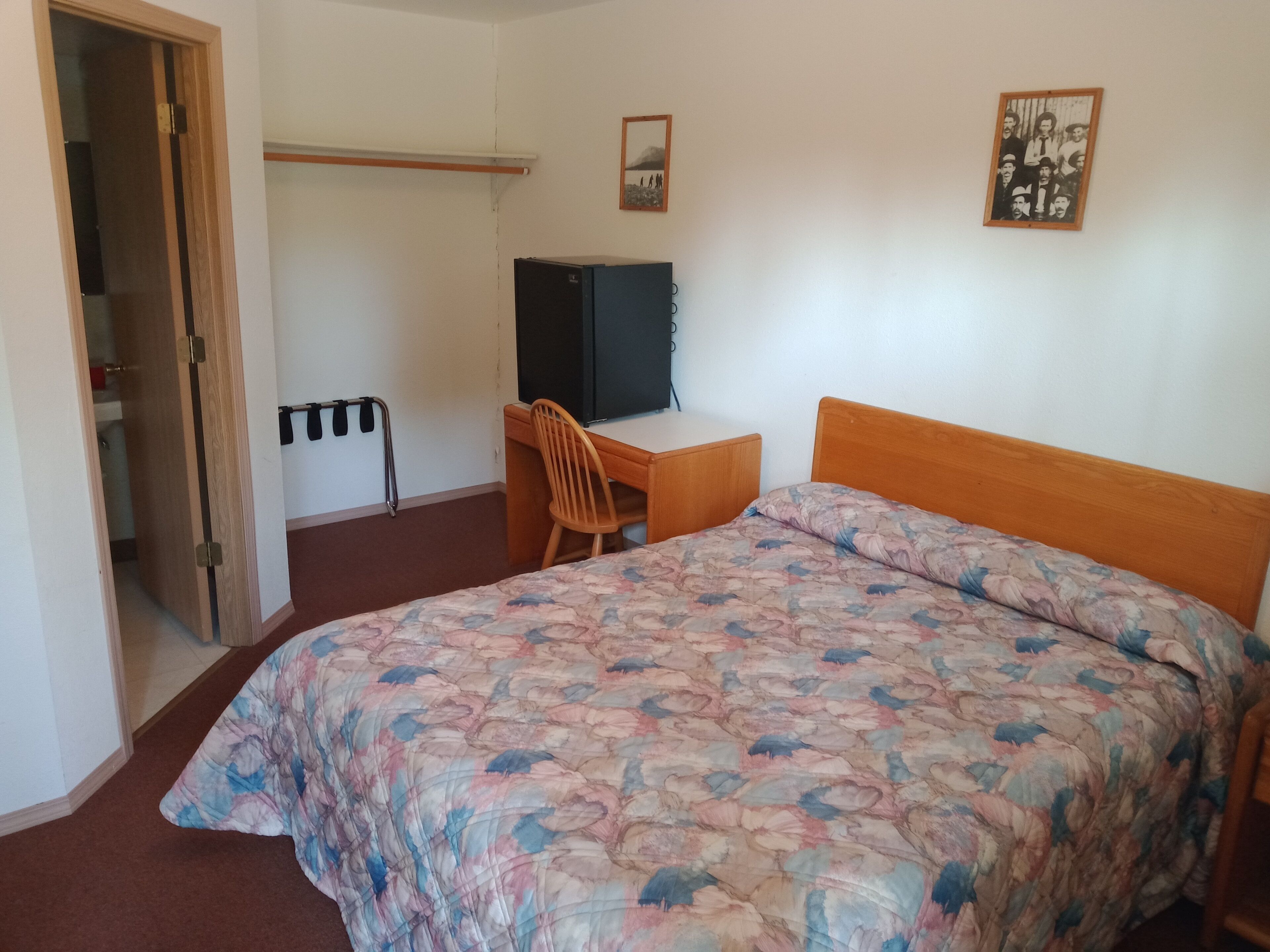 A bedroom with a bed, a desk, a chair, a wardrobe, and a picture on the wall.
