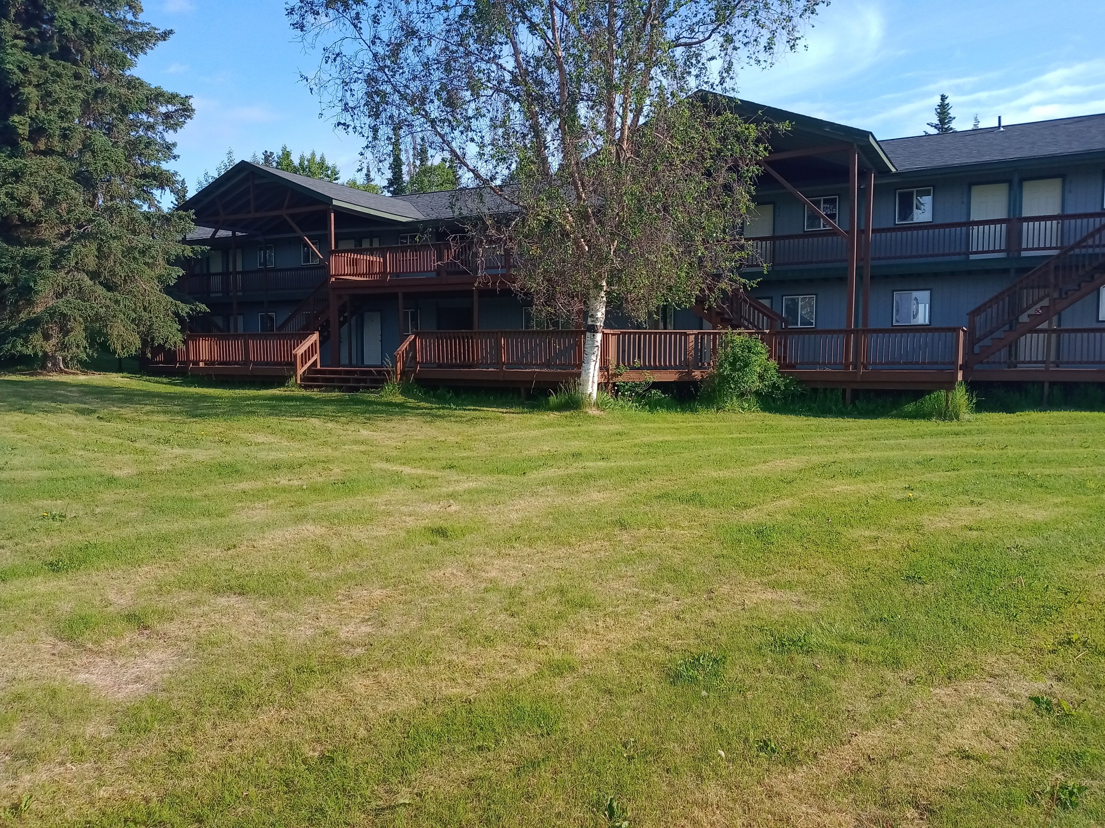 A two-story building with a wooden deck and a grassy yard.