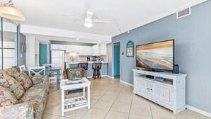 A living room with a sofa, a TV, a dining table, and a kitchen in the background. - Aqua Villa 302 (Fort Walton Beach)