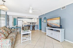 A living room with a sofa, a TV, a dining table, and a kitchen in the background. - Aqua Villa 302 (Fort Walton Beach)